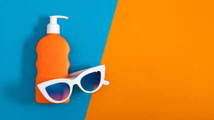 Stylish white glasses and orange bottle of sunscreen lotion on orange and blue background. Sun cream. Flat lay.