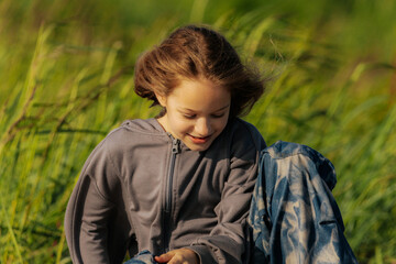 A smiling girl sits on a weathered log in a grassy field, wearing star-patterned pants and a gray...