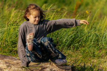 A smiling girl sits on a weathered log in a grassy field, wearing star-patterned pants and a gray...