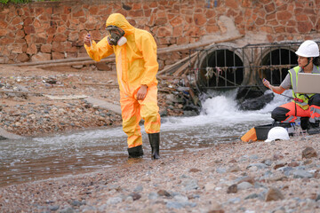 Environmental field team in protective gear analyzes water samples on a polluted beach. One holds a...