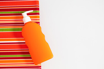 Bottle of sunscreen on striped lounge chair. Summer beach concept. Orange tube of sunscreen close-up.