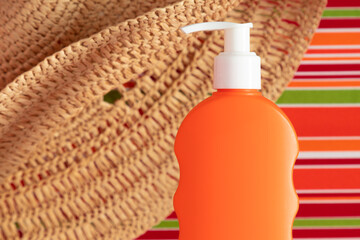 Close-up of an orange tube of sunscreen and a straw hat on a bright striped lounge chair. Sun protection. Top view