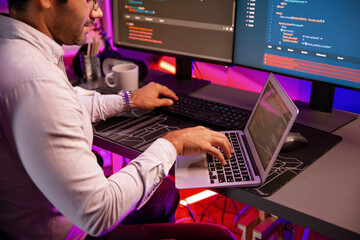 Smart IT developer working on laptop to type searching in software coding system at neon light...