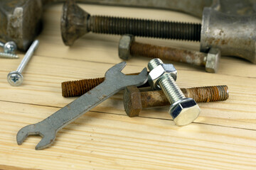 A collection of various bolts, nuts, and a wrench on a wooden surface. Tools are metallic with different sizes and conditions, showcasing hardware elements.