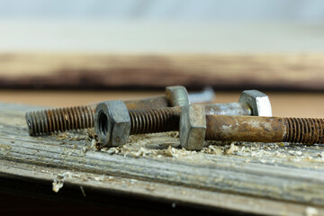 Close-up of metal bolts and nuts on a wooden surface. The scene includes threaded parts and wood...