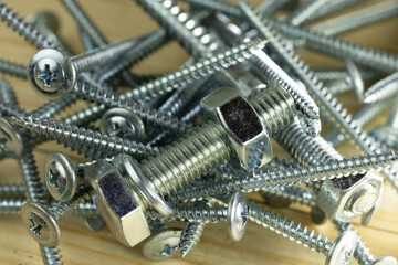 A close-up of various screws and bolts scattered on a wooden surface. The metal fasteners vary in size and shape, showcasing their threaded designs.