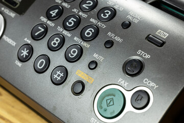A close-up view of a retro telephone with an answering machine. The device features a numeric keypad, buttons for fax and copy, and a mute function.