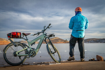 Male cyclist with a touring e-bike on a shore of frozen Horsetooth Reservoir in Colorado foothills.