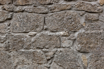 fragment of masonry with gray uneven stones bonded with cement mortar to form a textured background