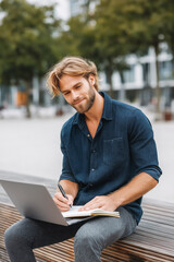 Thoughtful entrepreneur working remotely on a city bench with laptop and notebook