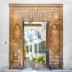 Old engraved archway with colorful city street behind in Cordoba, Spain