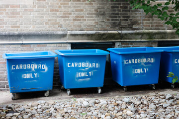 Blue bins designated for cardboard recycling located outside a building amidst a rocky landscape