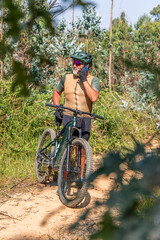 Senior cyclist talking on phone while riding electric mountain bike in forest