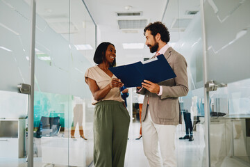 Business man and woman reviewing documents together in office hallway