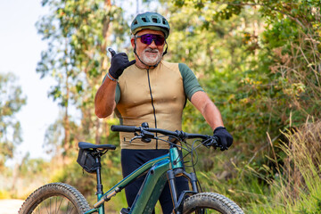 Senior cyclist showing thumbs up while riding electric mountain bike in forest