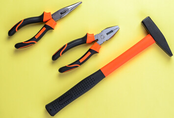 Hand tools including hammer and pliers on vibrant yellow background for repair concept