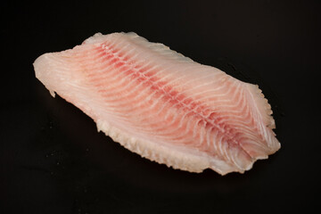 Fresh tilapia fillet on black background, top view.