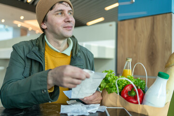 Man checking receipt after grocery shopping with paper bag full of healthy food, budgeting, personal finance, organic vegetables, modern lifestyle.