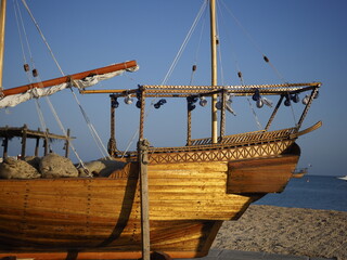 Golden dhow on shore, intricate details, clear blue sky.