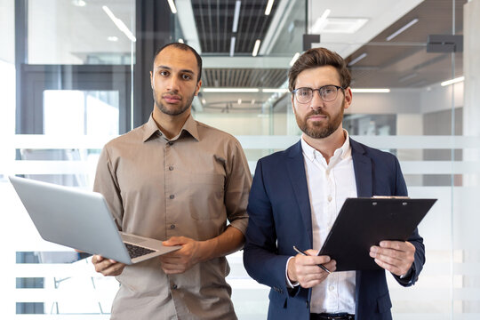 Fototapeta Two diverse business professionals standing confidently in a modern office setting, ready for business.