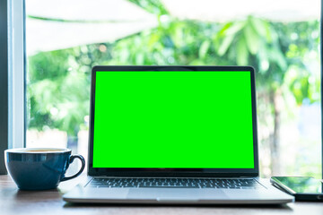 Mockup of laptop computer with empty screen with coffee cup and smartphone on table of the coffee shop background,Green screen