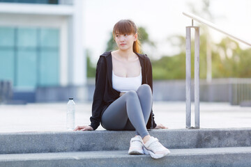 Portrait of beautiful asian Young woman in Black robe sportswear and drinks water working out outside. training on public equipment in outdoor at park. concept Exercise Healthy lifestyle.