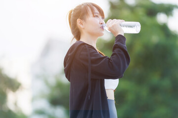 Portrait of beautiful asian Young woman in Black robe sportswear and drinks water working out outside. training on public equipment in outdoor at park. concept Exercise Healthy lifestyle.