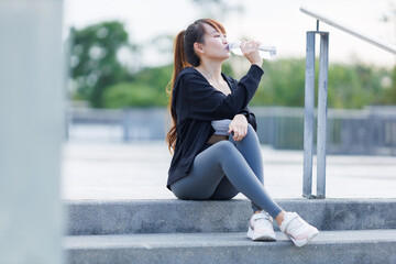 Portrait of beautiful asian Young woman in Black robe sportswear and drinks water working out outside. training on public equipment in outdoor at park. concept Exercise Healthy lifestyle.