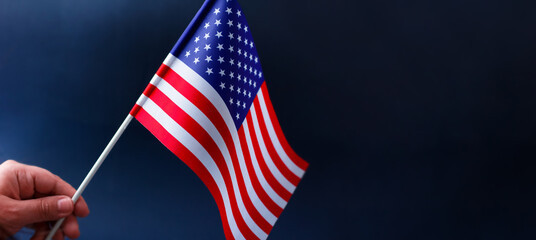 hand holding the flag of America on a dark blue background with copy space