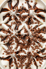 Close up of Vanilla ice cream with chocolate sauce and chocolate pieces in a paper container on a beige table. Food background.
