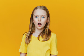 Surprised girl with blue eyes in a yellow shirt against a vibrant yellow background, expressing...
