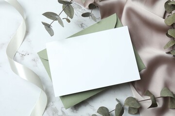Romantic flat lay witn paper envelope, blank card, eucalyptus branches and a ribbon on marble. Ideal for wedding invitations, event announcements, or feminine branding