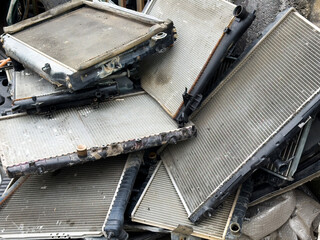 Old used car radiators stacked in scrapyard, automotive waste recycling, vehicle parts disposal, metal salvage, damaged cooling systems, industrial junk and spare parts.