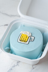 Small bento cake with blue cream cheese frosting decorated with a glass of foaming beer drawing in a gift box. Trendy cake as a gift for a beloved man