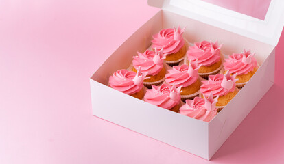 Beautiful cupcakes with pink whipped cream cheese topping. A box of birthday cupcakes on a pink pastel background. Festive dessert delivery concept