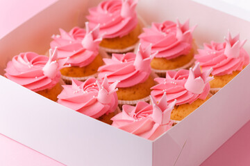 Beautiful cupcakes with pink whipped cream cheese topping. A box of birthday cupcakes on a pink pastel background. Festive dessert delivery concept