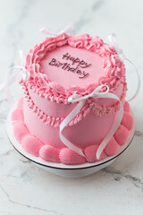Delicate lambeth style birthday cake with pink cream cheese frosting decorated with cream tracery and happy birthday text on top. White background