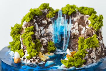 Beautiful birthday cake in the shape of an island decorated with chocolate edible mountains,...