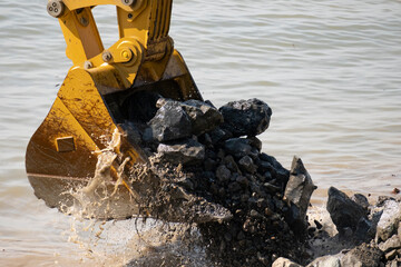 Construction equipment scoops rocks from the water at a construction site during daylight hours...
