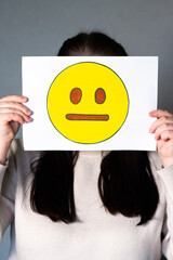 Woman holding emoji mask without smile and any expression in front of face. Social media trends, Gen Z marketing, World emoji day 17 July.