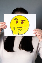Woman holding thinking emoji with index finger near mouth mask in front of face. Social media trends, Gen Z marketing, World emoji day 17 July.