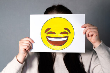 Woman holding happy smiling emoji mask in front of face. Social media trends, Gen Z marketing, World emoji day 17 July.