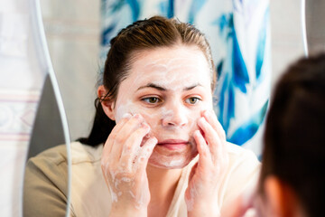 Morning skincare routine. Female cleansing her face with foam in bathroom. International self care day.