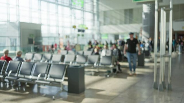 Blurred scene at airport terminal with defocused people and empty chairs under bright light.