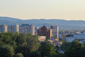 Obraz premium Panoramic view of Novi Sad, Serbia, featuring modern residential buildings, lush greenery, and distant mountains under soft evening light.