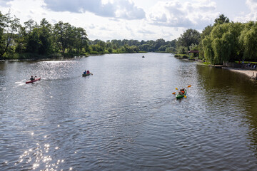 Group of kayakers paddling on river in summer day from rear view