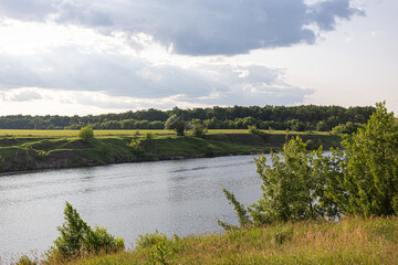 Calm river landscape with green meadows and trees under cloudy sky
