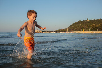 Happy little boy in orange shorts at sea on the beach in summer