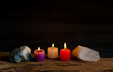 Velas encendidas de colores junto a cristales y piedras naturales sobre superficie de madera en...