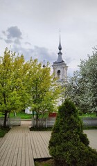 Naklejka premium Church of Varlaam of Khutynsky Ilyinsky parish surrounded by flowering trees. Bell tower of ancient Orthodox Church and spring greenery. Russia, Vologda, May 23, 2025